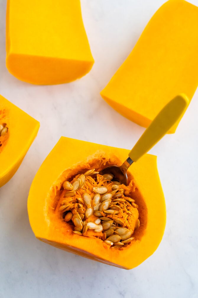Halfways cut butternut squash with a spoon in the seeds and guts.