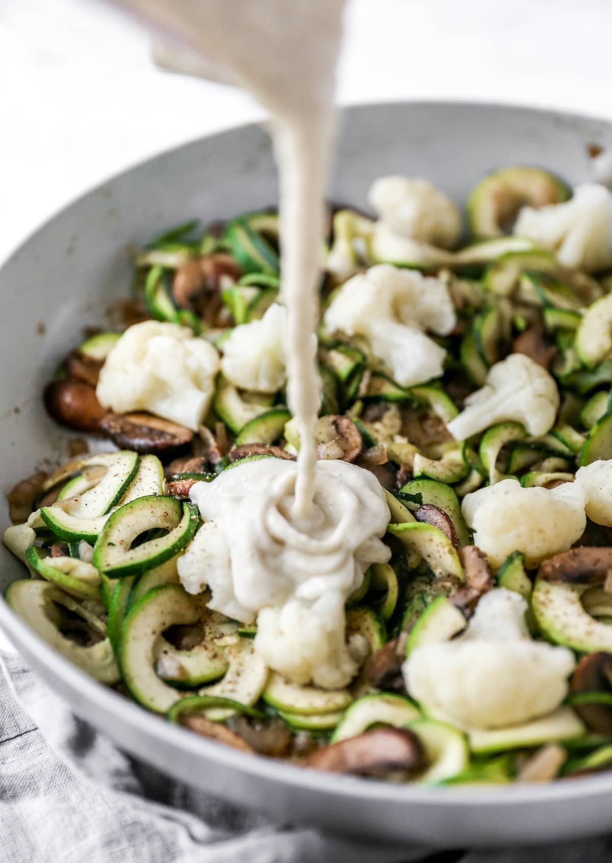 Cauliflower alfredo sauce drizzling over zucchini noodles and mushrooms.
