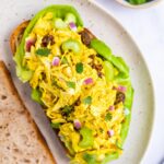 Curry chicken salad on an open faced sandwich with sourdough bread. Bowl of cilantro in the background.