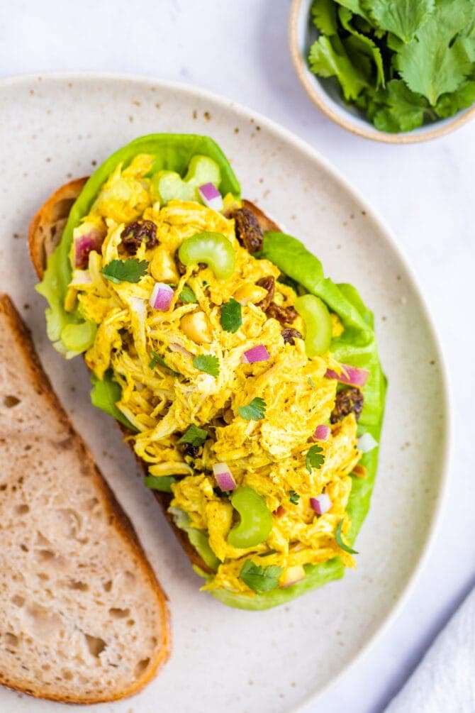 Curry chicken salad on an open faced sandwich with sourdough bread. Bowl of cilantro in the background.