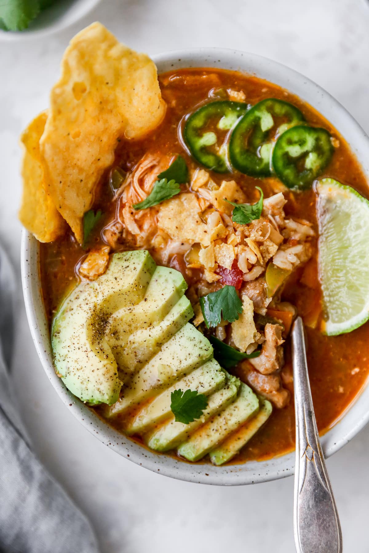 Bowl of chicken tortilla soup topped with jalapeños, lime, avocado and tortilla chips.