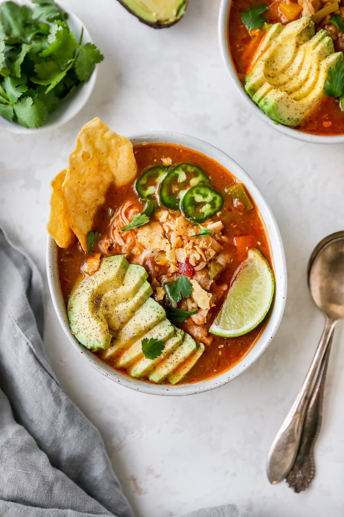 Bowl of chicken tortilla soup with avocado, line, jalapeno and chips as garnish.