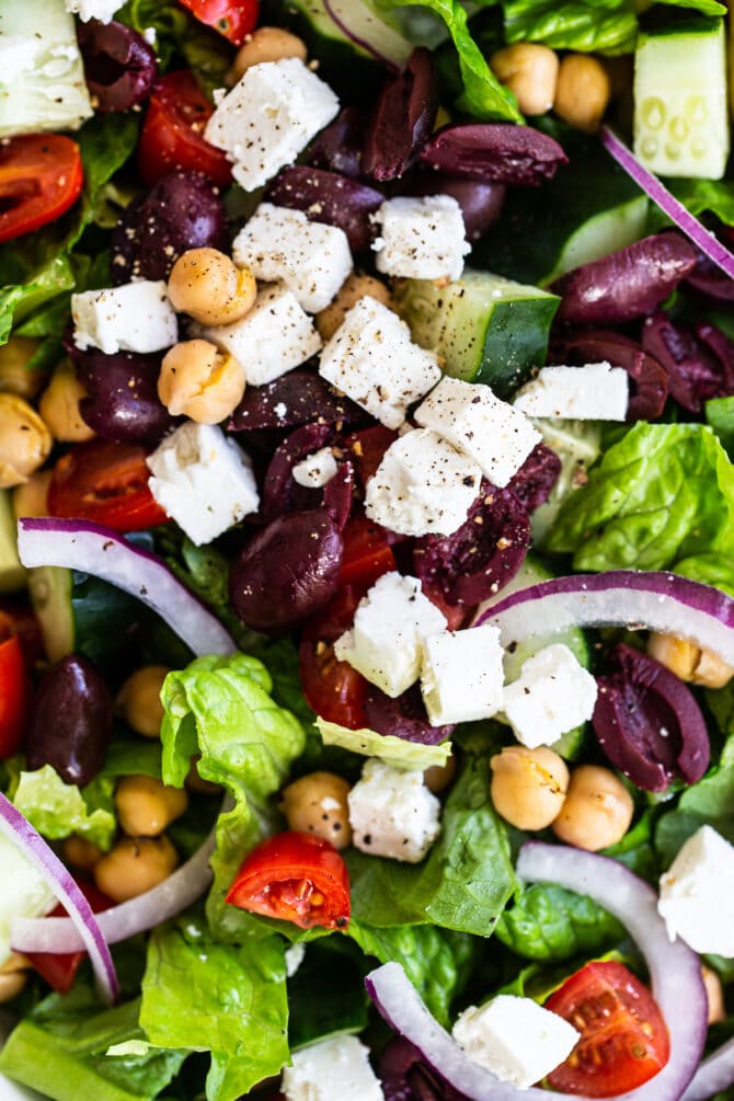 Close up photo photo of a greek salad with romaine, kalamata olives, tomatoes, chickpeas, feta, cucumber and onions.