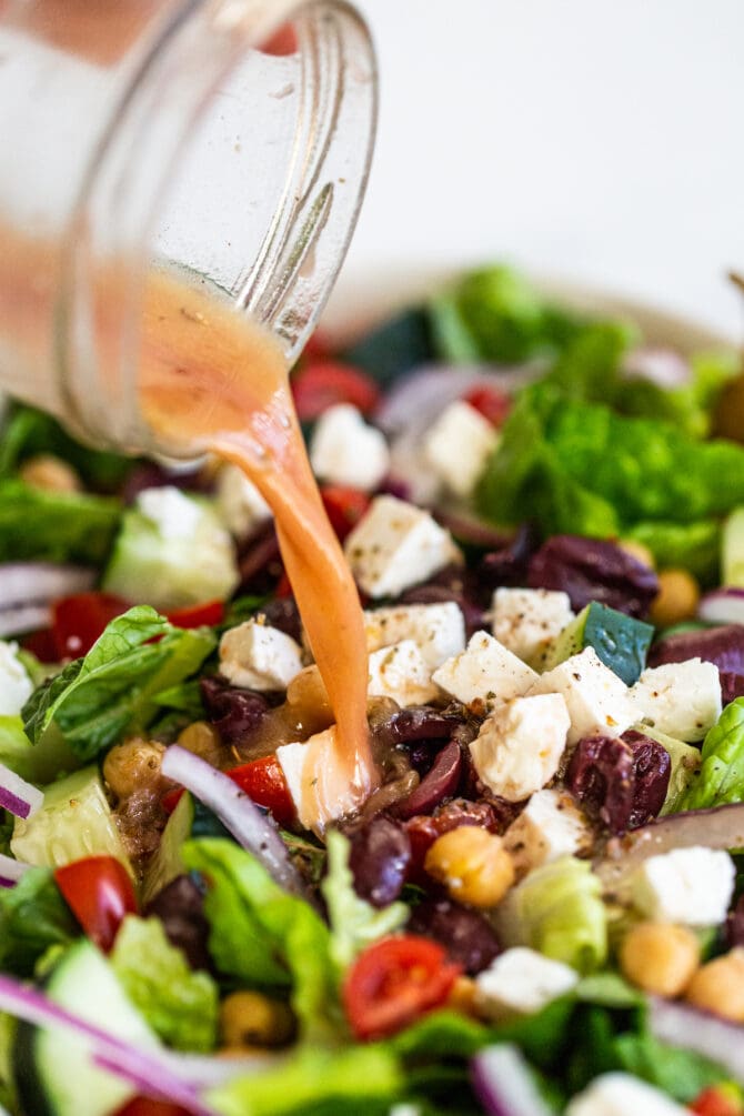 Homemade greek salad dressing being drizzled over a Greek salad.