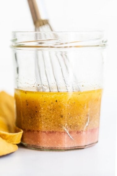 Jar of greek salad dressing with a little whisk.