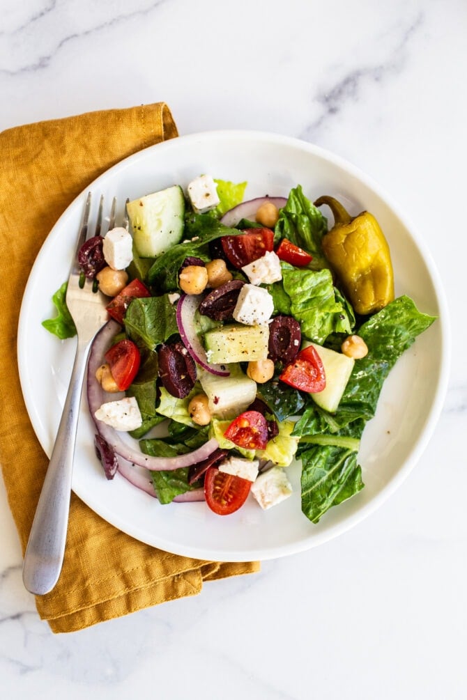 Plate and fork with greek salad. Yellow cloth napkin is below the plate.