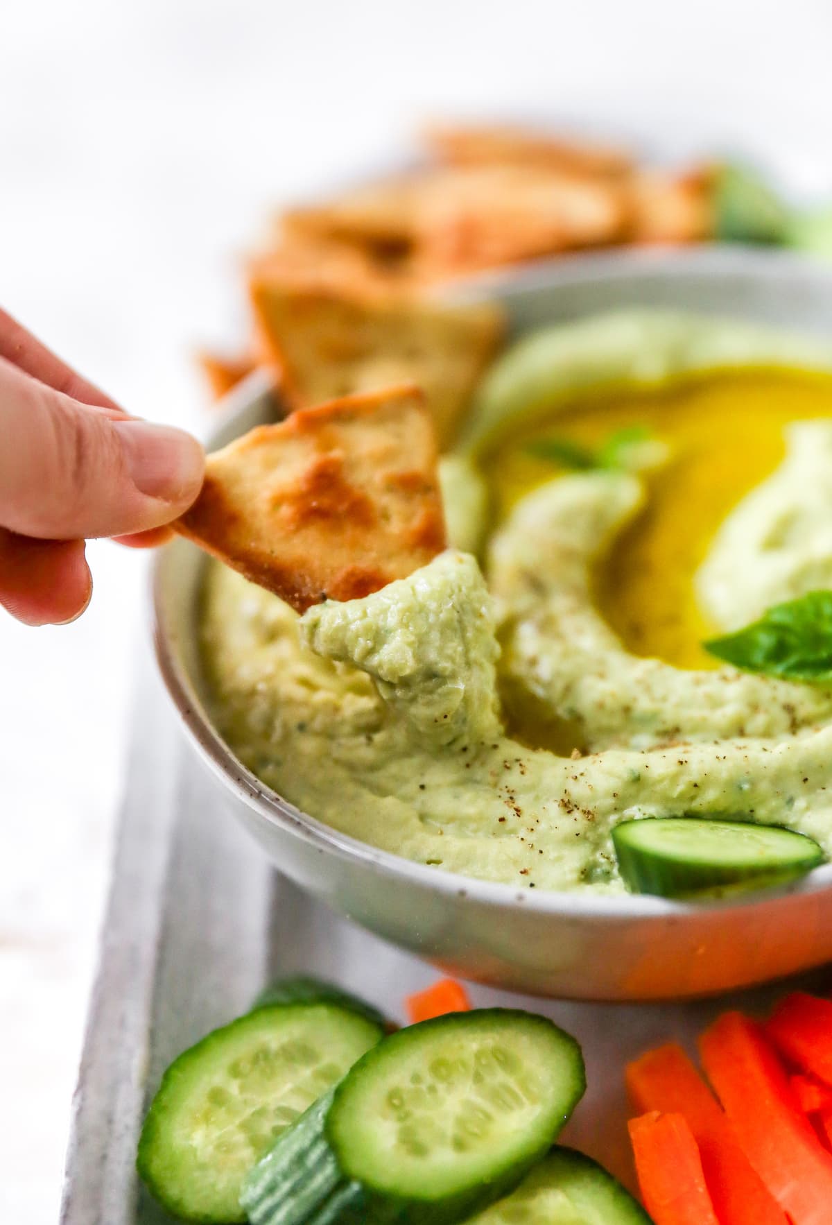 Hand dipping a pita cracker into a bowl of lima bean hummus.