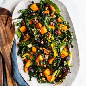 Oval serving tray with kale and butternut salad. Wood salad tongs are beside the plate.