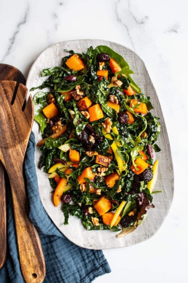 Oval serving tray with kale and butternut salad. Wood salad tongs are beside the plate.