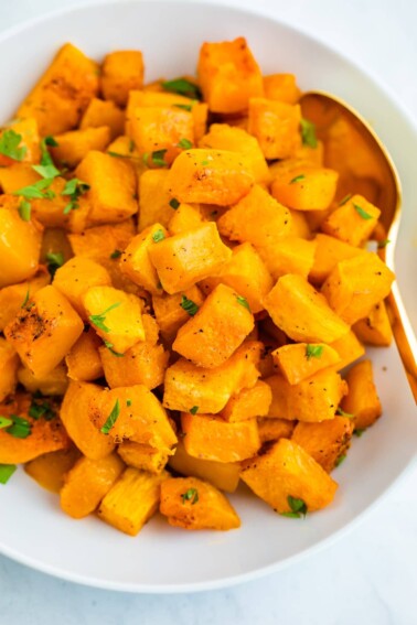 Bowl of roasted butternut squash topped with chopped herbs.