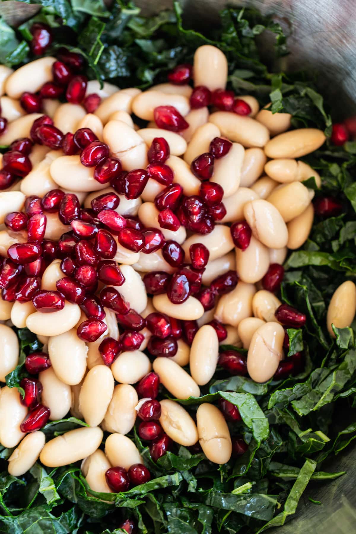 Kale, white beans and pomegranates in a mixing bowl.