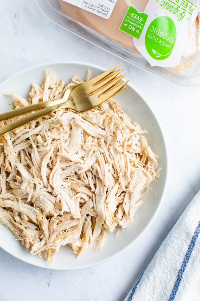 White plate with shredded chicken and two gold forks. Organic chicken container in the background