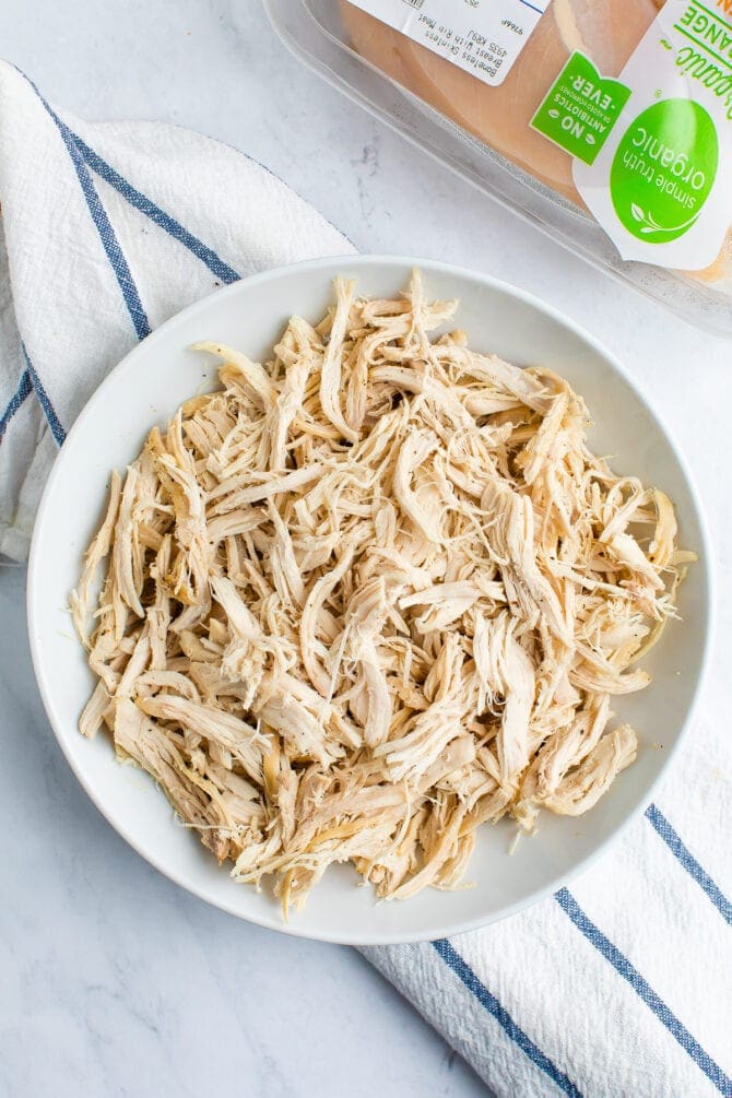 White plate with shredded chicken. Organic chicken container in the background