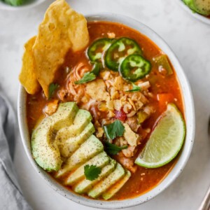 Bowl of chicken tortilla soup with avocado, line, jalapeno and chips as garnish.