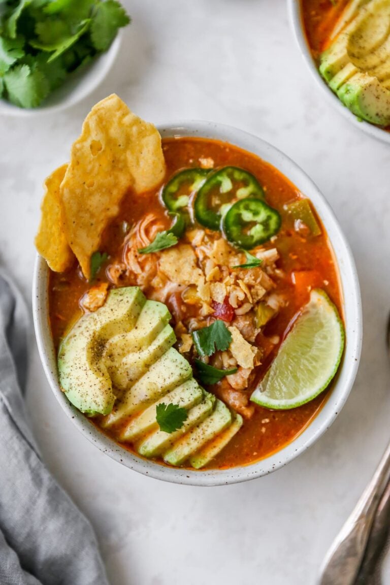 Bowl of chicken tortilla soup with avocado, line, jalapeno and chips as garnish.