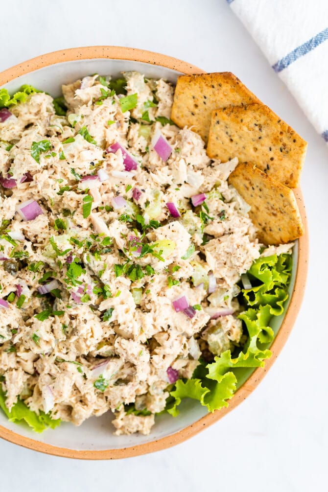 Bowl with tuna salad served over lettuce and served with crackers.