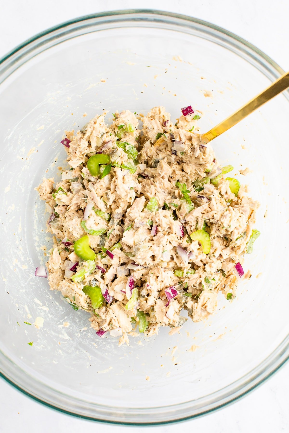 Spoon mixing up tuna salad in a mixing bowl.