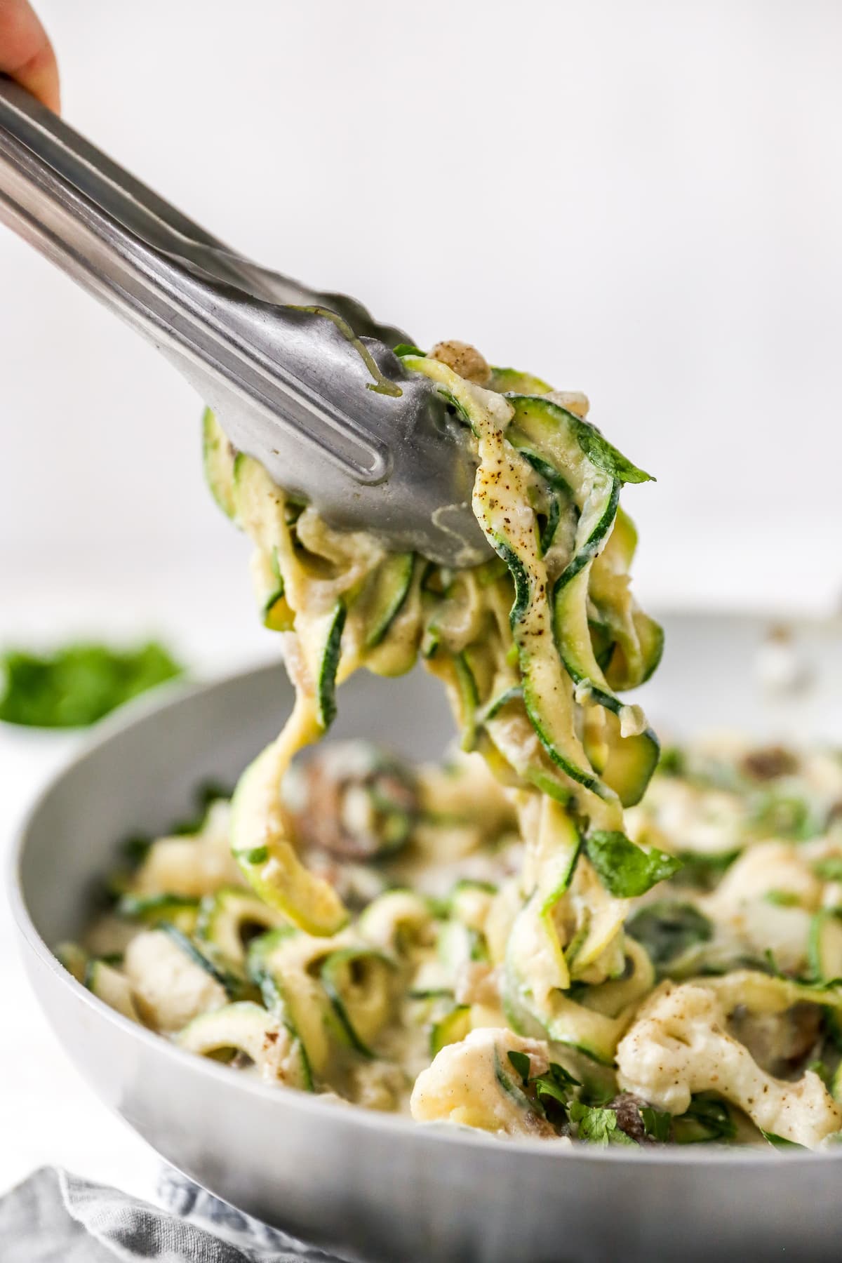 Tongs grabbing some zucchini noodles.