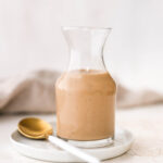 Glass jar full fo creamy balsamic salad dressing. A spoon is next to the jar.