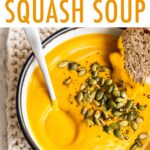 Soup bowl with butternut squash soup, a spoon and some bread.