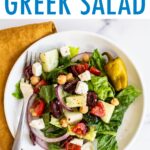 Plate of greek salad. Fork is on the plate and a cloth napkin is below the plate.