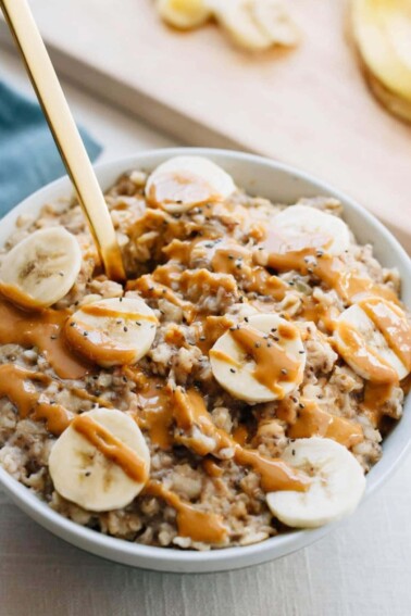 Bowl of oatmeal topped with peanut butter, banana slices and chia seeds.