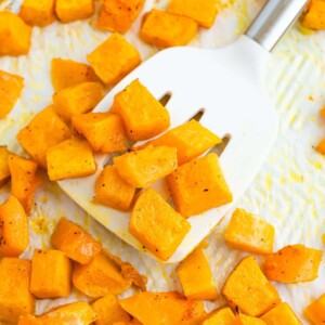 Spatula lifting up some roasted butternut squash cubes from a sheet pan.