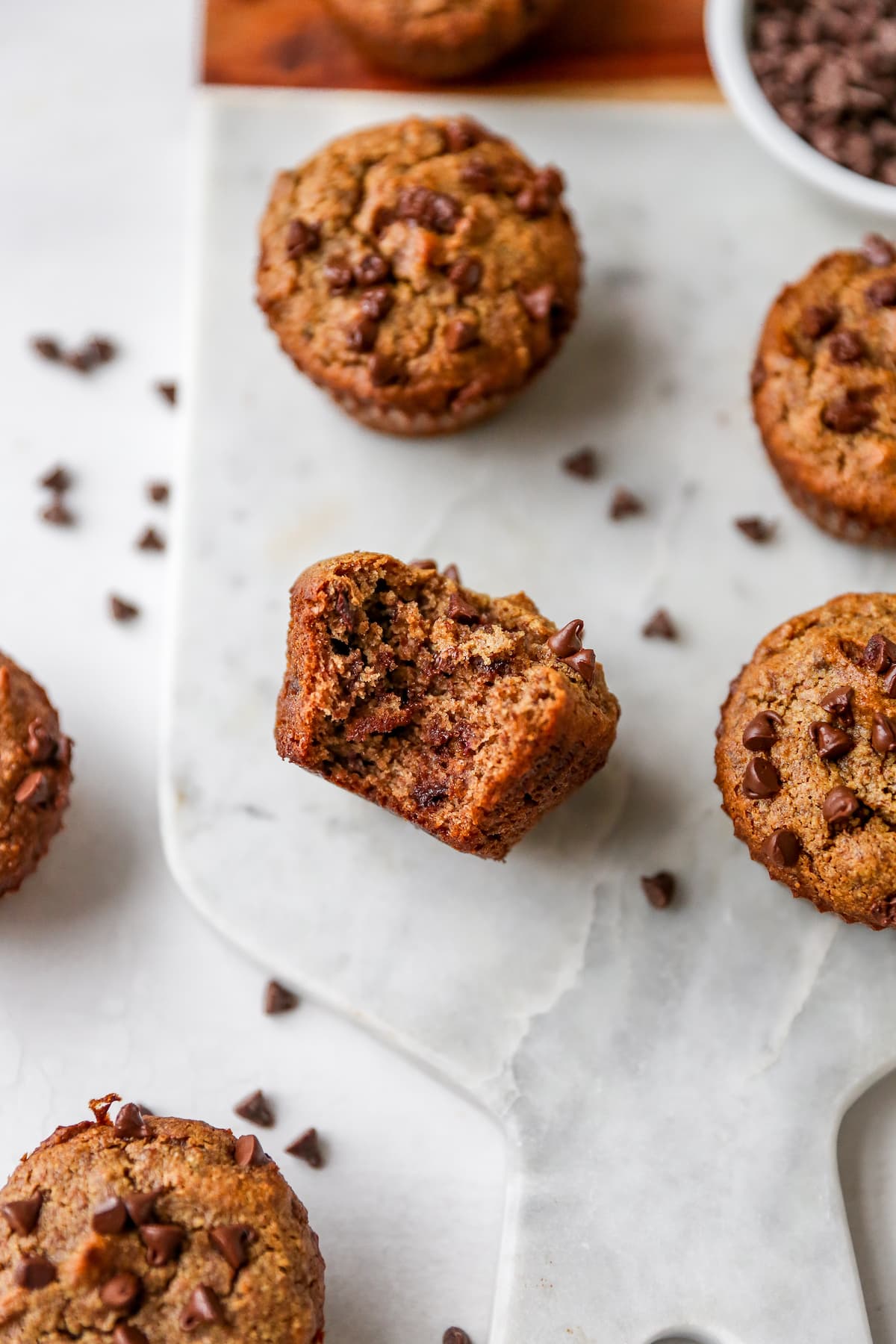 Almond flour muffins on a marble board. One has a bite taken out of it.