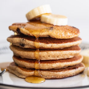 Stack of banana chocolate chip pancakes topped with banana slices and maple syrup.