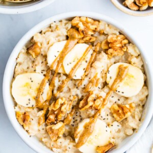 Bowl of oatmeal topped with walnuts, banana slices and peanut butter.