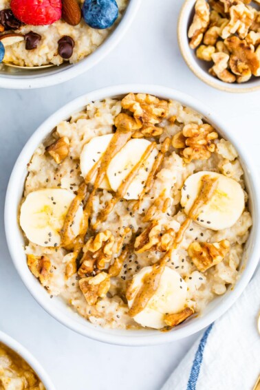 Bowl of oatmeal topped with walnuts, banana slices and peanut butter.