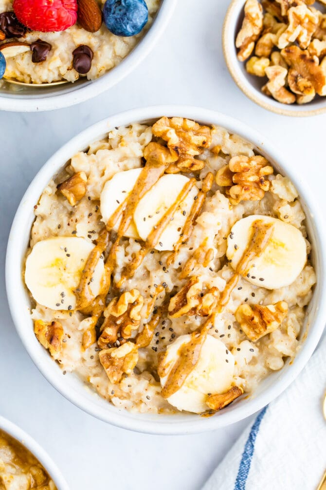 Bowl of oatmeal topped with walnuts, banana slices and peanut butter.