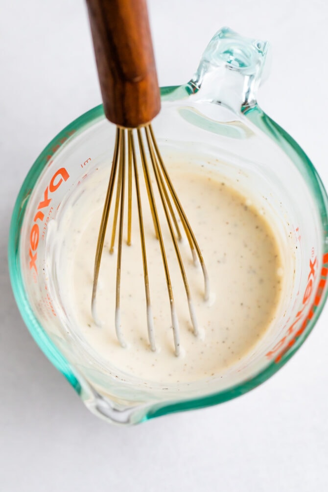 Glass container with creamy dressing and a whisk.