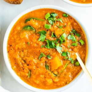 Bowl of butternut red lentil stew topped with parsley. Crusty bread is beside the bowl.