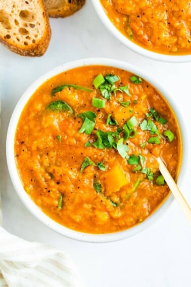 Bowl of butternut red lentil stew topped with parsley. Crusty bread is beside the bowl.