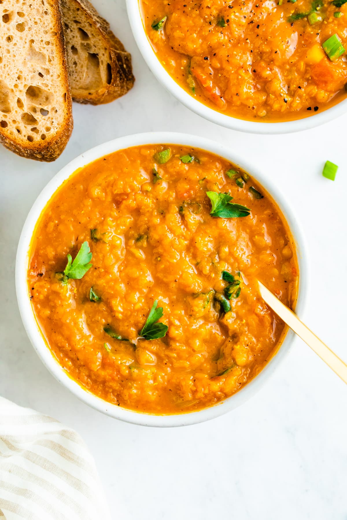 Bowl of butternut red lentil stew topped with parsley. Crusty bread is beside the bowl.