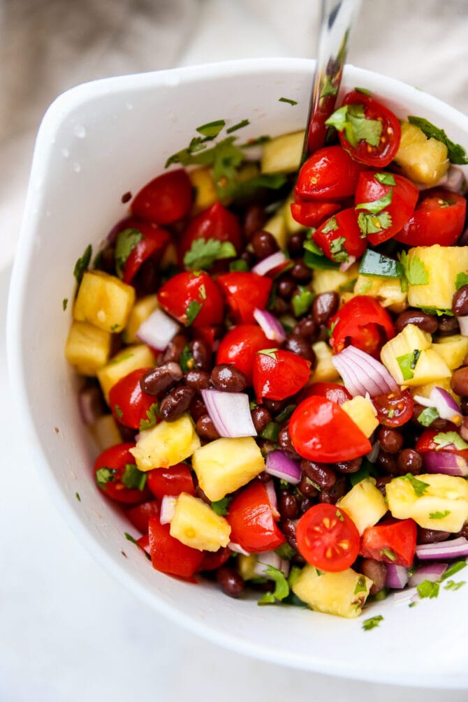 Bowl of pineapple, tomato and black bean salsa with a spoon.