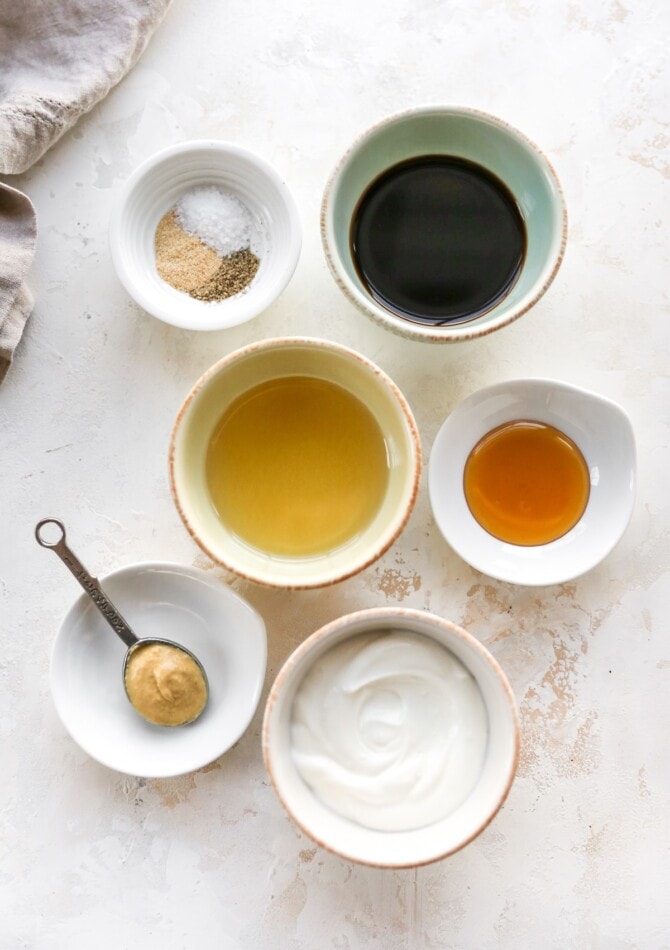 Spices, balsamic dressing, oil, honey, greek yogurt and mustard measured out into bowls.