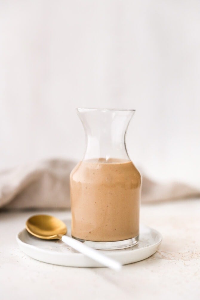 Glass jar full fo creamy balsamic salad dressing. A spoon is next to the jar.