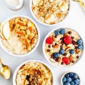 Four bowls of oatmeal with toppings like bananas, nuts, apples, berries, chocolate chips and brown sugar.