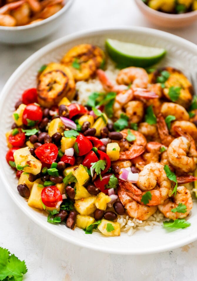 Plate with rice, pineapple salsa, jerk shrimp and plantains with lime and cilantro for garnish.