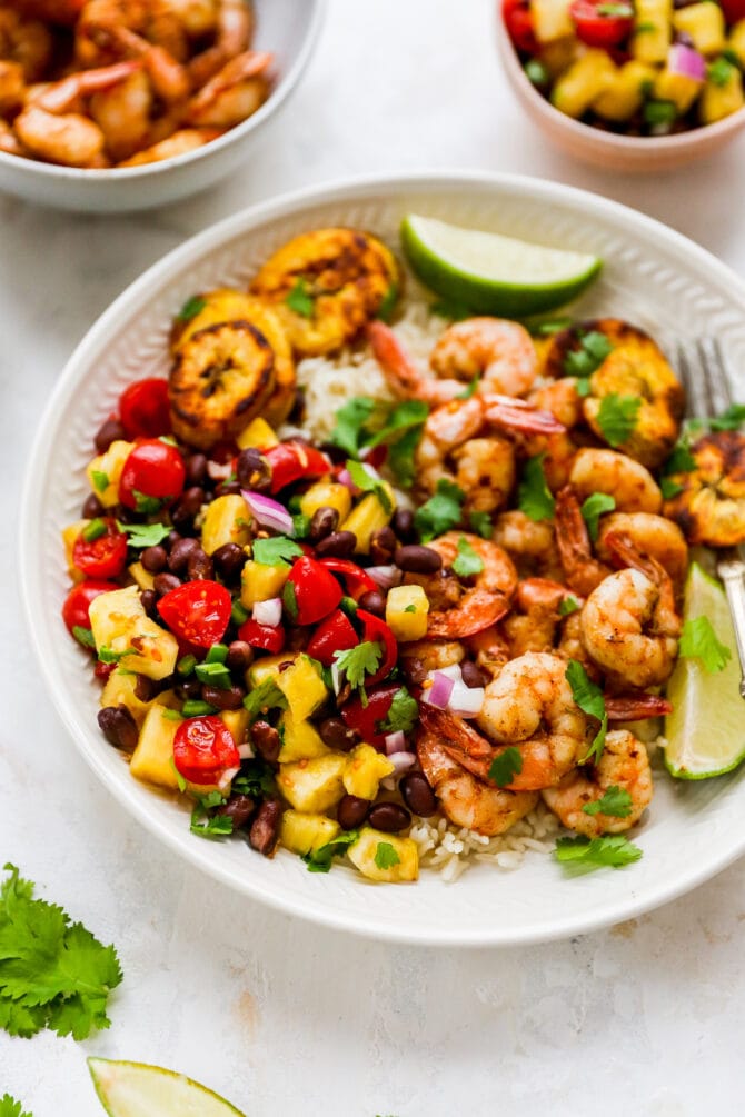 Plate with rice, pineapple salsa, jerk shrimp and plantains with lime and cilantro for garnish.