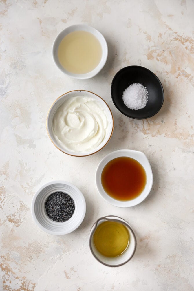 Ingredients like oil, maple syrup, salt, greek yogurt and poppyseeds measured in little bowls.