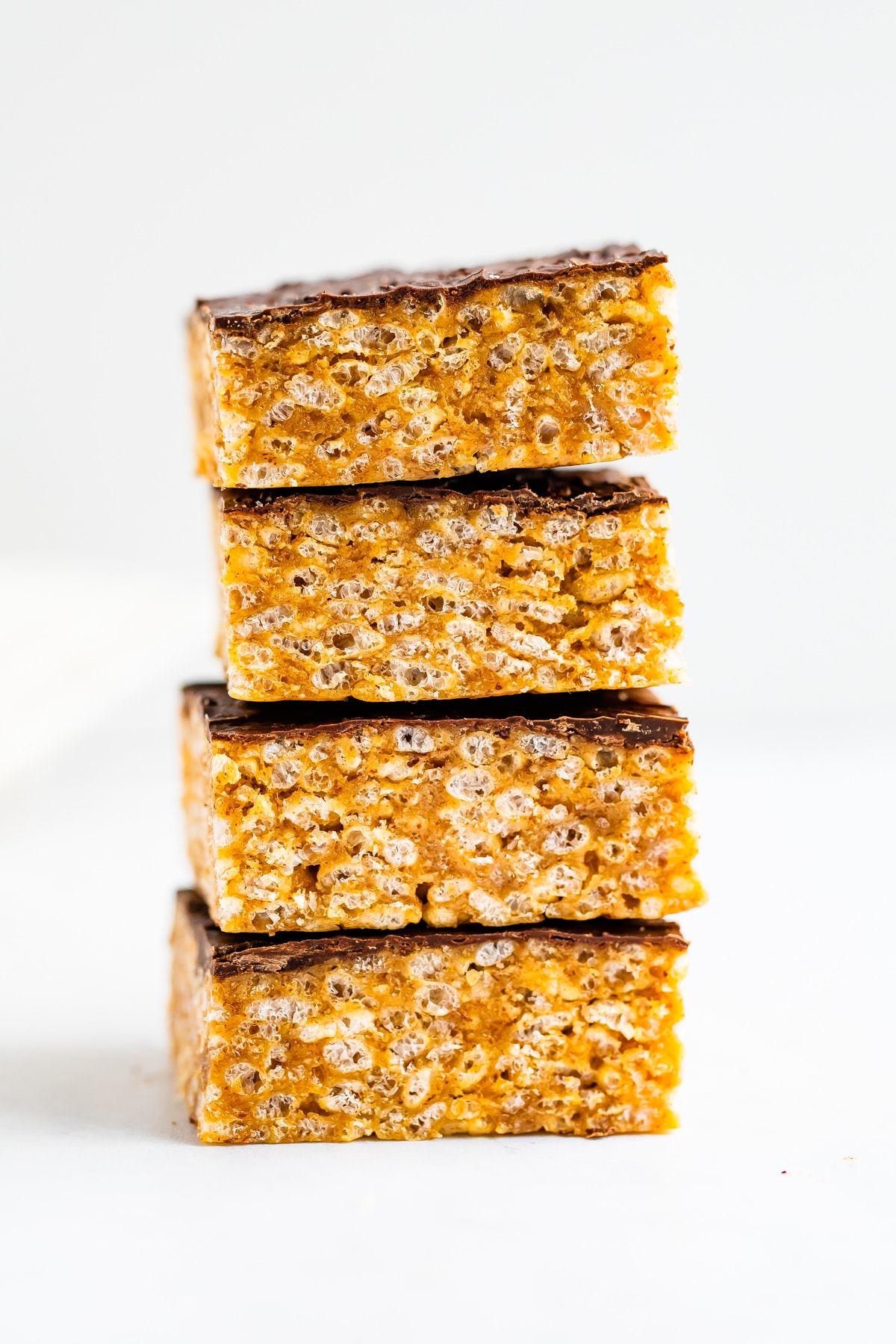 Stack of four rice krispie treats with a layer of chocolate on top.