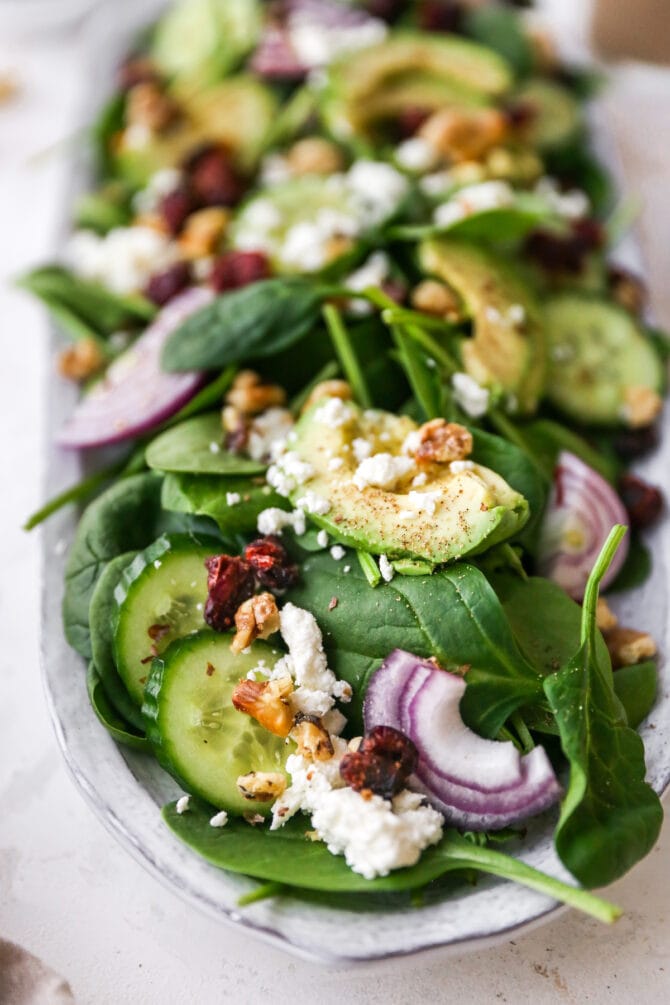 Spinach salad on a serving platter with cheese, nuts, onions and cranberries.