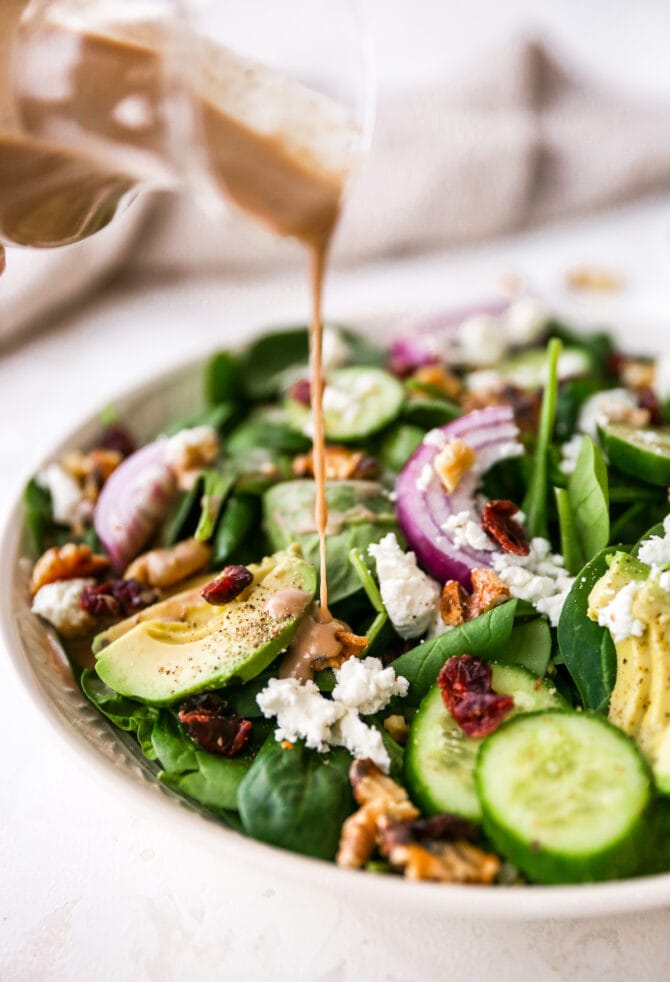 Creamy balsamic vinaigrette dressing being poured over a spinach salad.