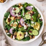 Plated spinach salad topped with avocado, goat cheese, cranberries, walnuts and onion.