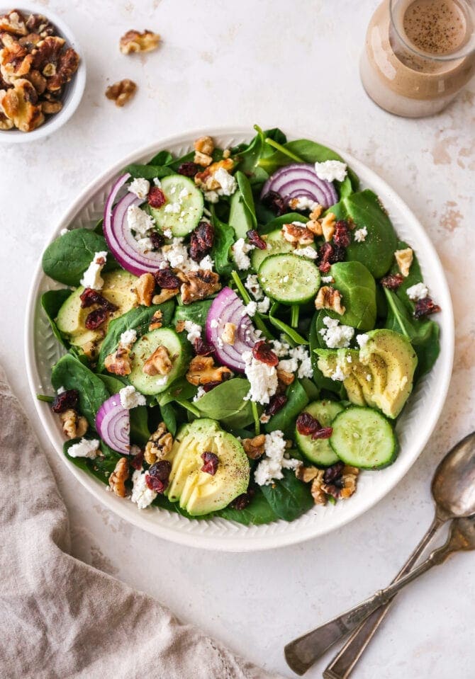 Plated spinach salad topped with avocado, goat cheese, cranberries, walnuts and onion.