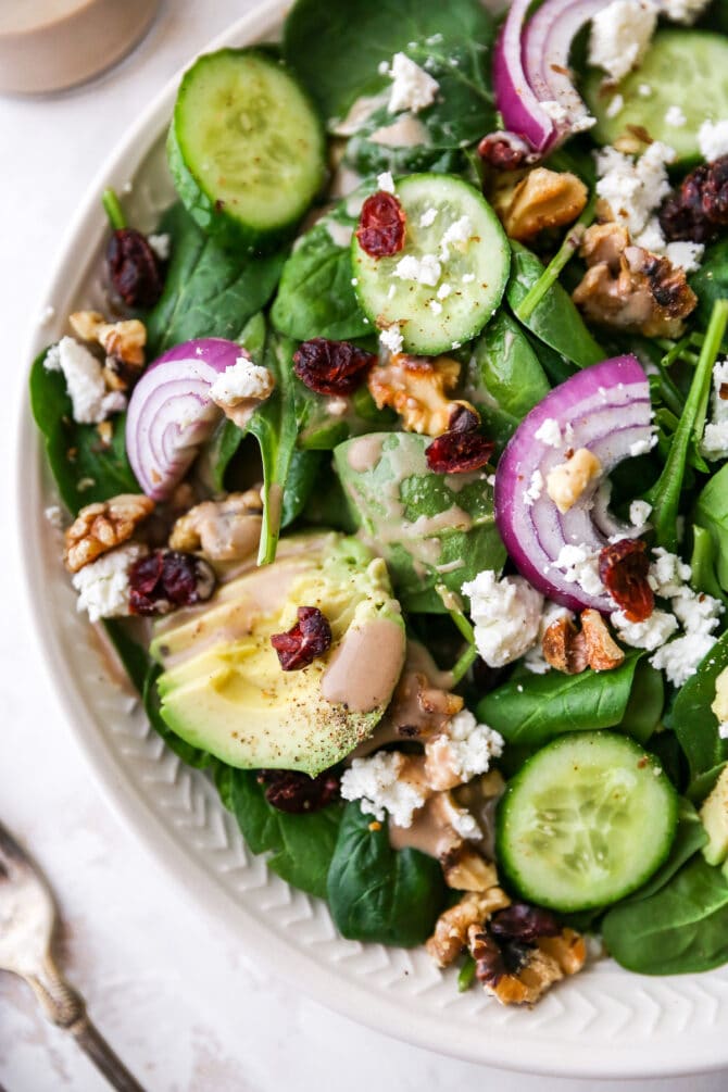 Plated spinach salad topped with avocado, goat cheese, cranberries, walnuts, onion and a drizzle of creamy balsamic dressing.