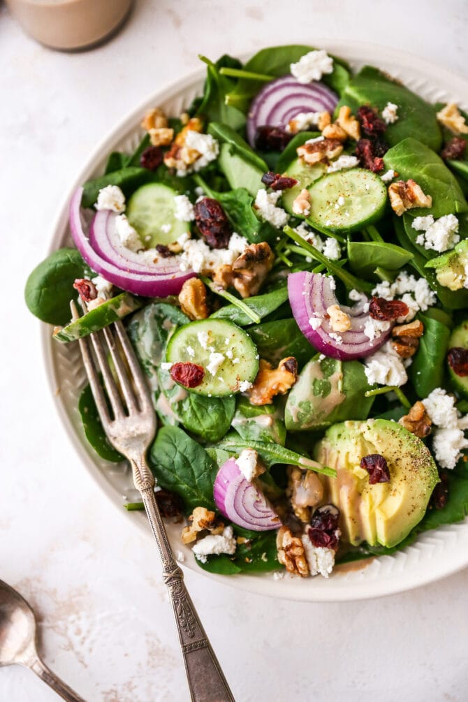 Plated spinach salad topped with avocado, goat cheese, cranberries, walnuts, onion and a drizzle of creamy balsamic dressing.